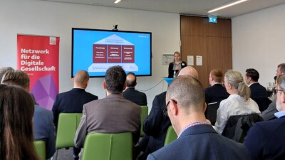 Christine Rupp spricht zu einer Gruppe von Menschen im Publikum, hinter ihr ein großer Bildschirm mit einer Präsentation.